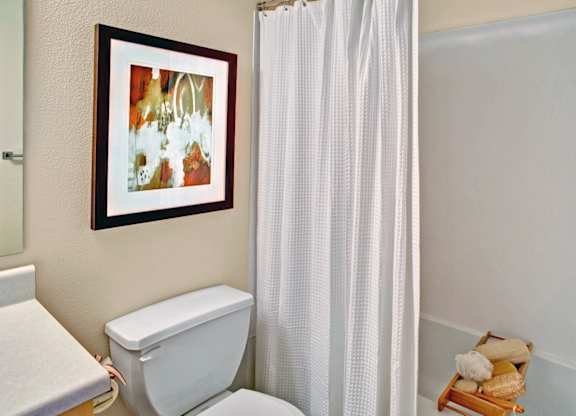 A white toilet sits next to a white shower curtain in a bathroom.