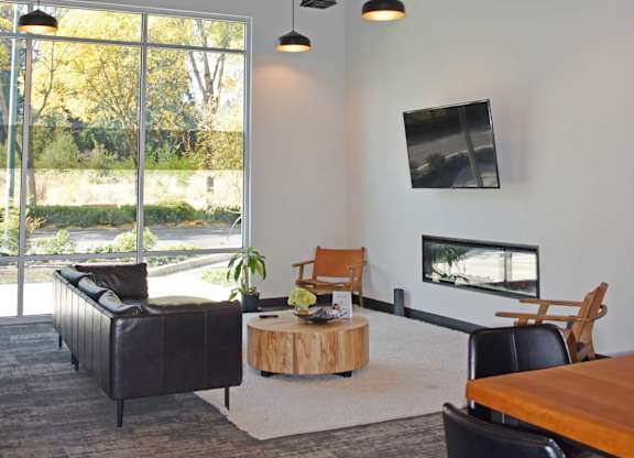 A modern living room with a black couch, a wooden coffee table, and a flat screen TV mounted on the wall at The Duo Apartments in University Place, WA..