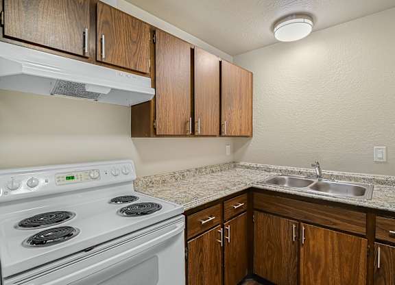 Apartment kitchen with white stove, wood cabinetry and counter space at The Lakes Apartments Moses Lake WA