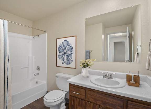 White bathroom with single-sink vanity, toilet, and large mirror in a 2 bed 1 bath apartment at the Lakes in Moses Lake Apartments