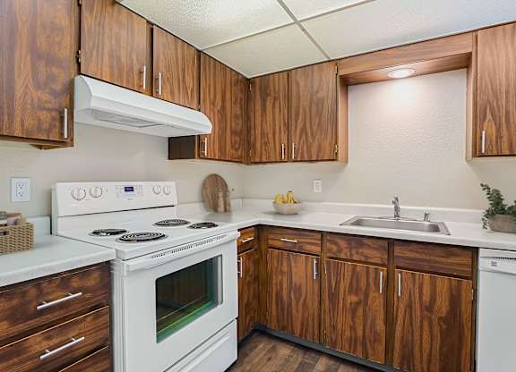 Kitchen with warm wood cabinets, white electric range, and ample counter space at The Lakes Apartments