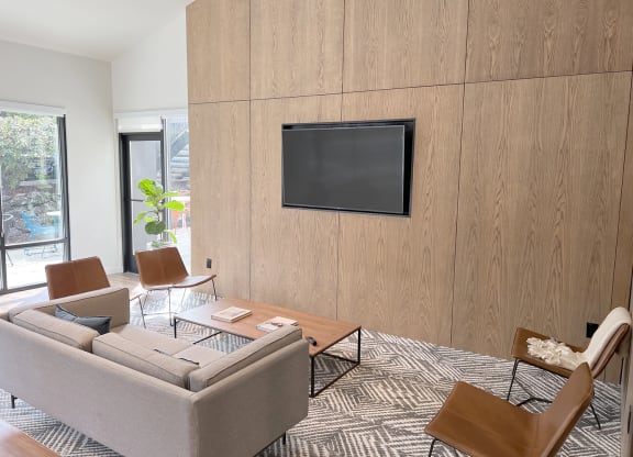 Clubhouse with floor to ceiling windows, a large flat-screen TV, a couch, 4 chairs, a coffee table, rug. The patio is visible from the clubhouse at University Glen, University Place