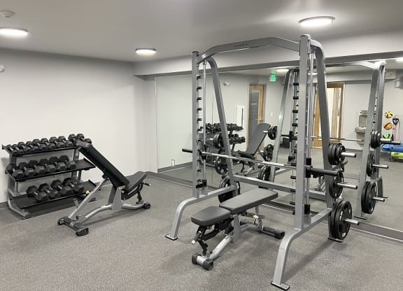 Fitness center with weight rack, free weights, squat, bench press rack, and two benches at University Glen, University Place, Washington