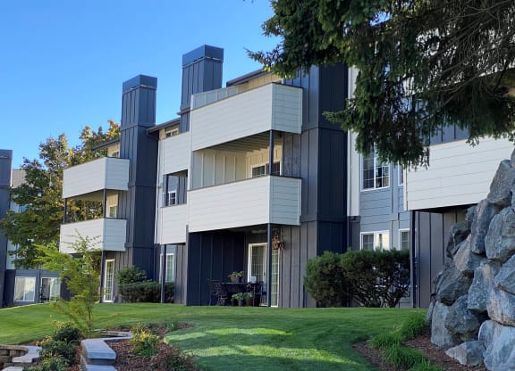 Apartments with balconies and patios are surrounded by manicured grass, landscaping, and trees at University Glen, University Place, WA, 98466