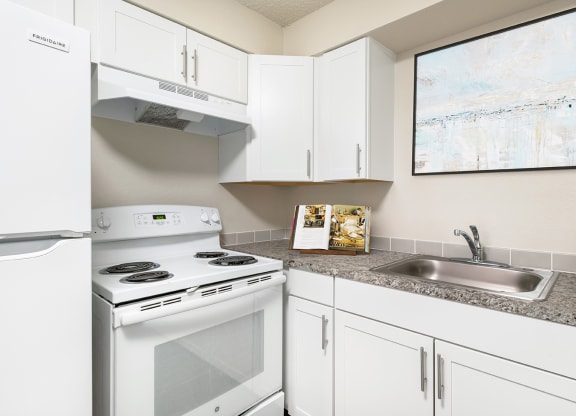 Corner of a kitchen with custom white cabinets, spacious countertops, a stainless steel sink, oven, stovetop and hood range, and full-size fridge.at Wildflower, Washington