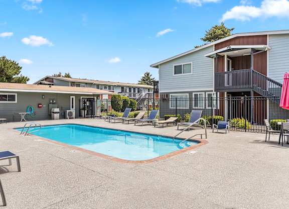 A swimming pool surrounded by lounge chairs and a building in the background t Wildflower Apartments in Kennewick, WA..