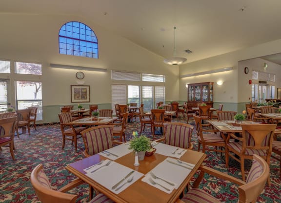 a dining room with tables and chairs and a large window at Hilltop Commons Senior Living, Grass Valley, CA