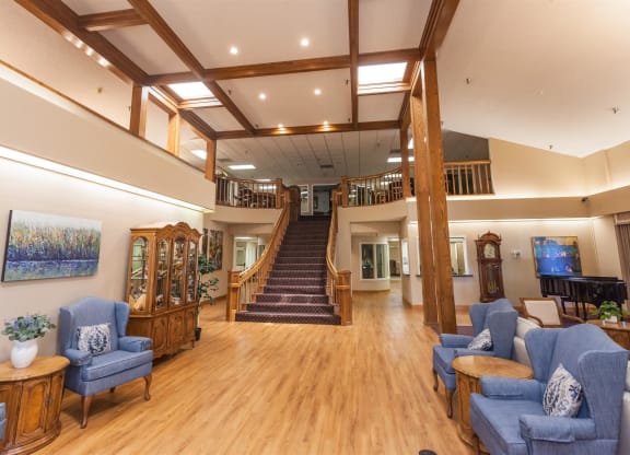 the lobby of a building with blue chairs and a staircase at River Commons Senior Living, Redding California