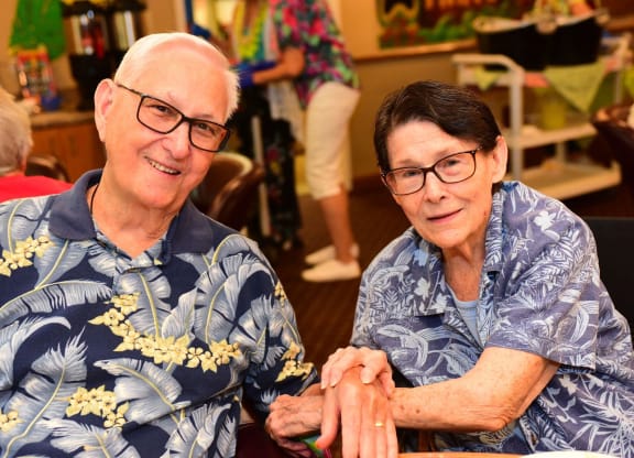 a man and a woman sitting at a table holding hands at River Commons Senior Living, Redding, CA
