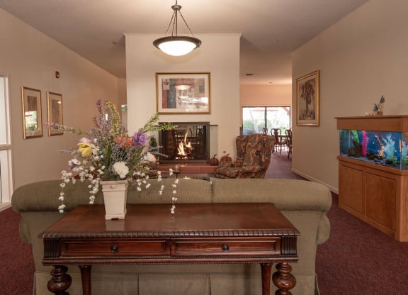 a living room with a fireplace and a table with flowers at Roseville Commons Senior Living, California, 95678