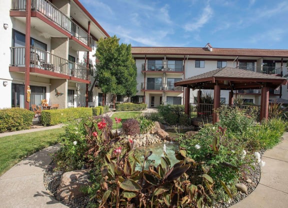a courtyard with a garden in front of an apartment building at Roseville Commons Senior Living, Roseville California