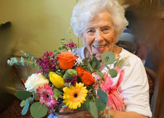 an elderly woman holding a bouquet of flowers at Winding Commons Senior Living, Carmichael, California