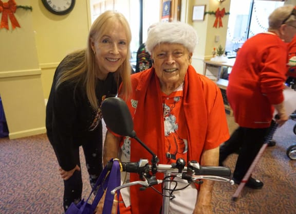 a woman is standing next to an older woman on a bike at Winding Commons Senior Living, Carmichael, CA