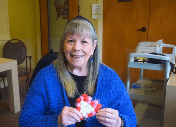 a woman sitting in a chair holding a piece of origami in her hands at Winding Commons Senior Living, Carmichael, 95608