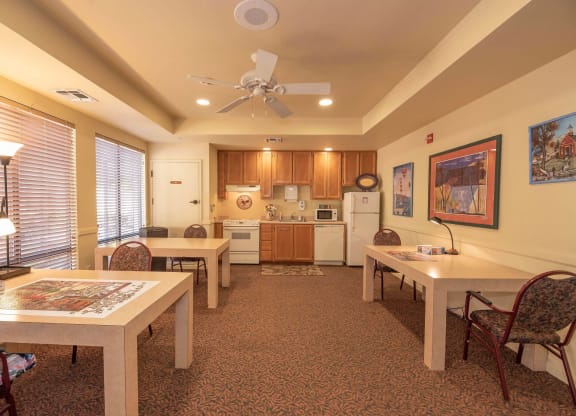 a dining room with tables and chairs and a kitchen with a ceiling fan at Winding Commons Senior Living, Carmichael