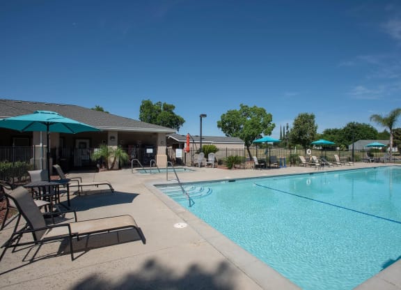 a swimming pool with chairs and umbrellas next to a building at Castle Vista Senior Duplex Community, Atwater, California