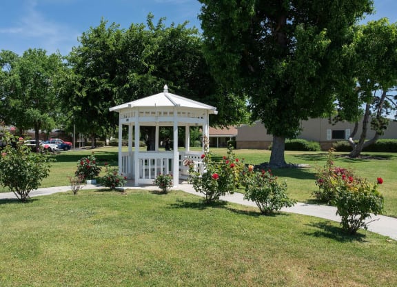 a white gazebo in the middle of a park with trees and flowers at Castle Vista Senior Duplex Community, Atwater, CA, 95301