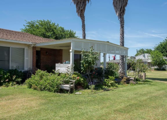 a house with a covered porch and a lawn and palm trees at Castle Vista Senior Duplex Community, Atwater, CA