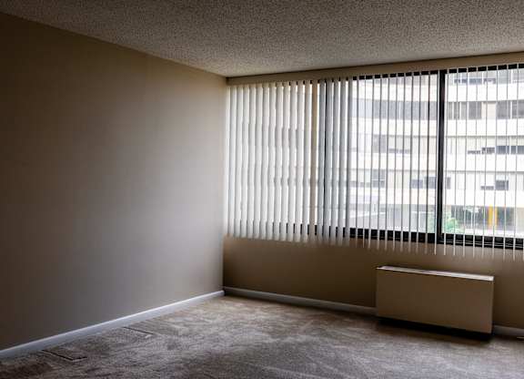 A room with a window covered by blinds and a radiator on the floor at Hampton Plaza Apartments, Maryland
