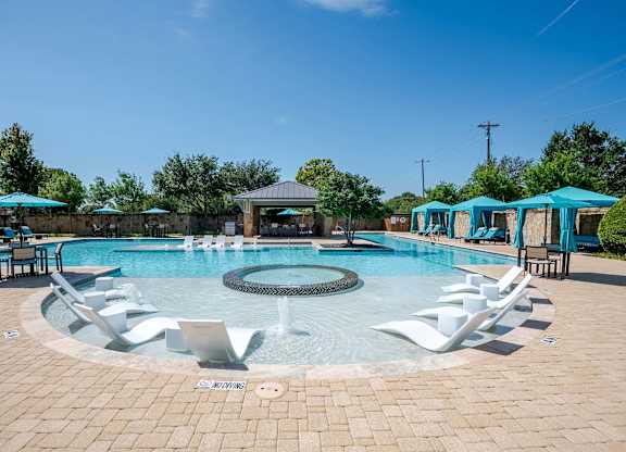a resort style pool with white chairs and blue umbrellas at Discovery at Craig Ranch, McKinney