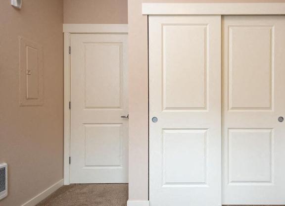 a closet with two white doors and a door to a hallway