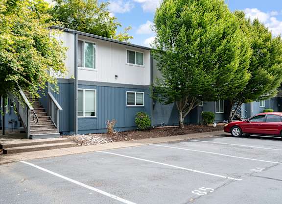 A red car is parked in a parking lot in front of a two-story building.