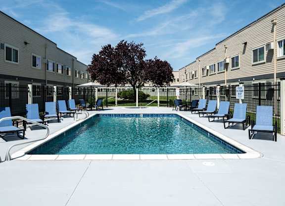 A swimming pool surrounded by chairs and a tree in a sunny courtyard.