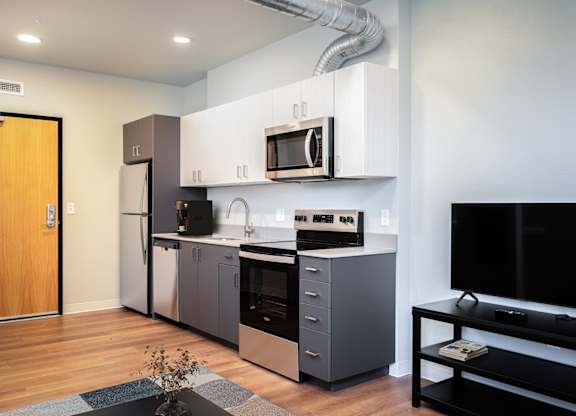 A modern kitchen with a refrigerator, oven, microwave, and a television.