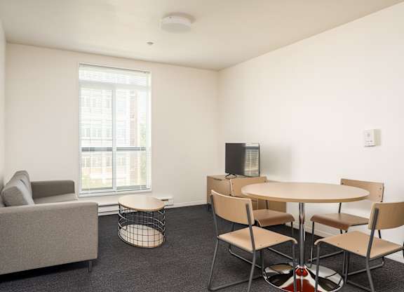 A living room with a grey couch, a round table with four chairs, and a television.