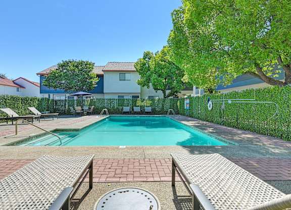 A pool surrounded by a brick patio and a metal fence.