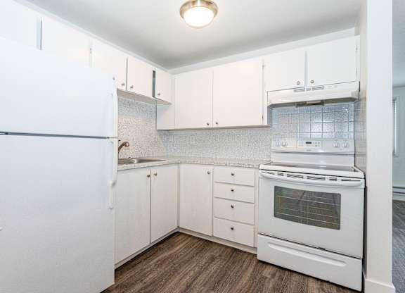 A white kitchen with a refrigerator, oven, and sink.