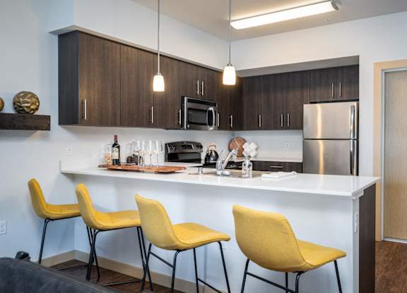 Dog-Friendly Apartments in Everett WA - The Waterline - Kitchen with Stainless Steel Appliances, Quartz Countertops, Dark Wood-Style Cabinetry, Pendant Lighting, Breakfast Bar, and Vinyl Hardwood Floo