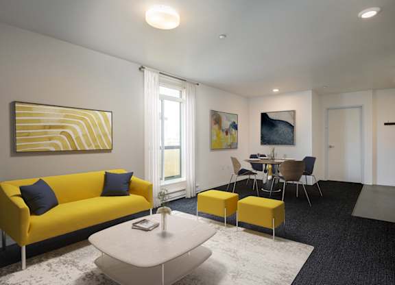 A living room with a yellow couch and a painting on the wall.