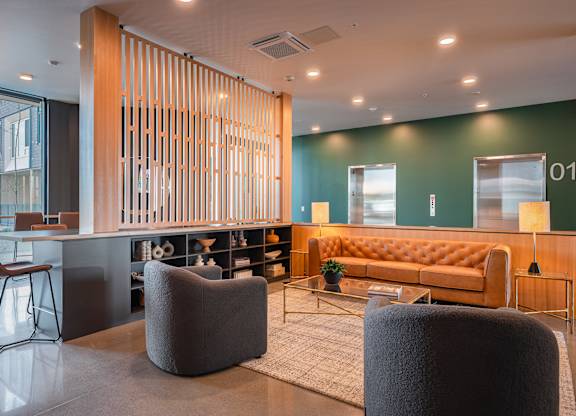 A modern lounge room with a wooden partition grey chairs and tan couch