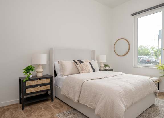 A bedroom with a bed, nightstand, and a plant.