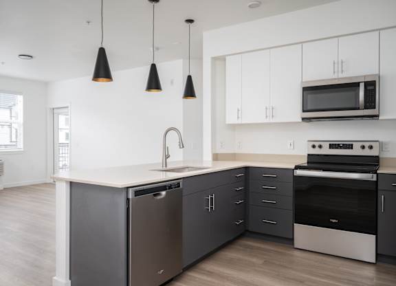 A modern kitchen with a stainless steel dishwasher and oven, a microwave above the stove, and pendant lights hanging from the ceiling.
