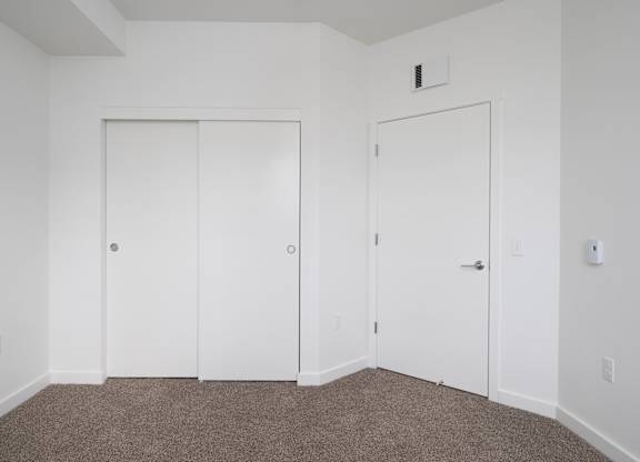 Two white doors in a room with carpeted floor.