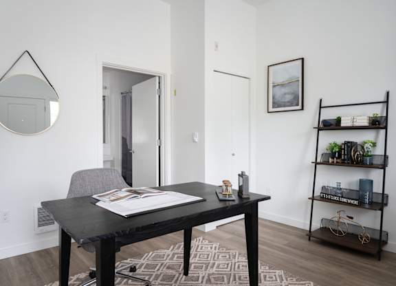 A black table with a grey chair and a round mirror on the wall.