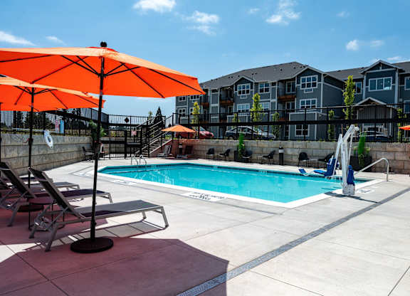A pool surrounded by chairs and umbrellas with apartment buildings in the background.