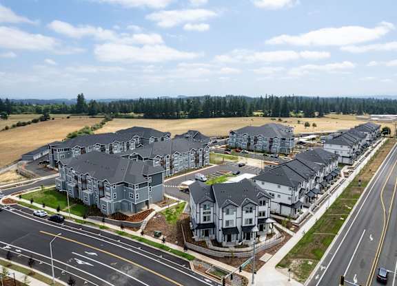 A row of houses are built on a street with a grassy field in the background.