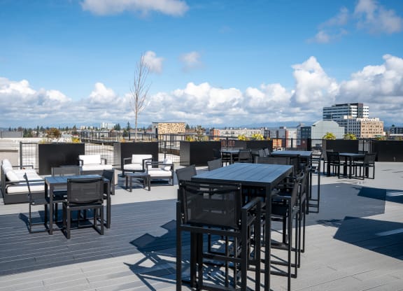 a rooftop patio with tables and chairs and a city in the background