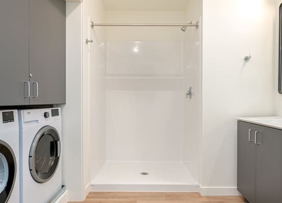 A white bathroom with a walk-in shower and a washer and dryer.