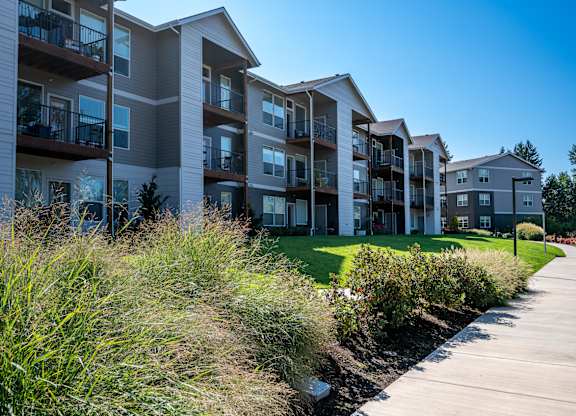 A row of modern apartment buildings with balconies and a walkway in front.