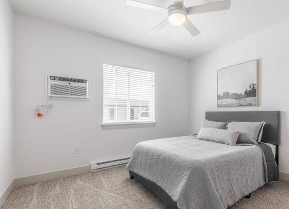 A bedroom with a bed, a window with blinds, a ceiling fan, and a painting on the wall.