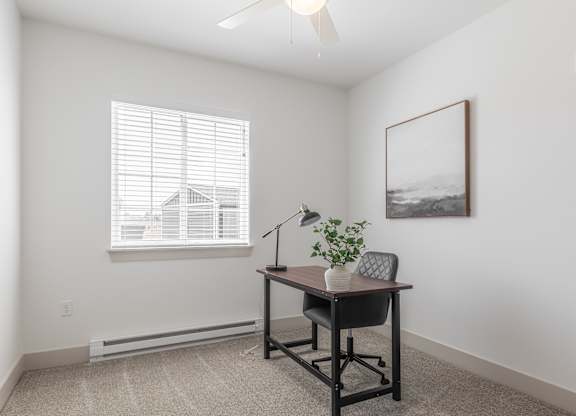 A room with a desk and chair, a plant, and a picture on the wall.