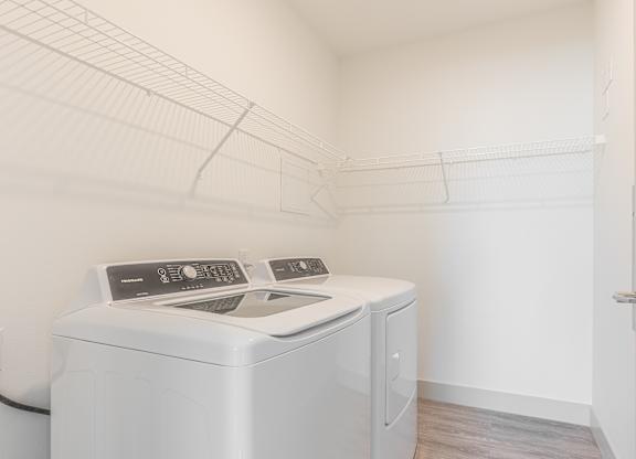 A white washing machine sits in a small, white-walled laundry room.