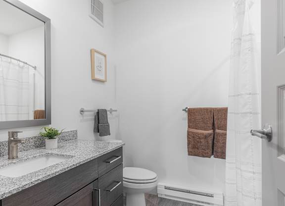 A bathroom with a white toilet, a sink with a mirror above it, and a towel rack with two brown towels.