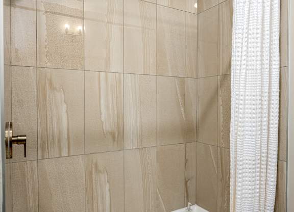 A bathroom with a beige tiled wall and a white shower curtain.
