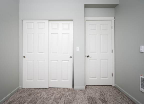 Two white doors in a room with carpeted floor.