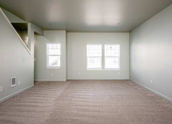 A large empty room with carpeted floor and two windows.